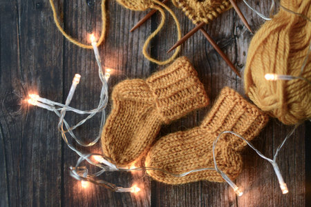 Knitted baby booties with Christmas lights on rustic wooden background