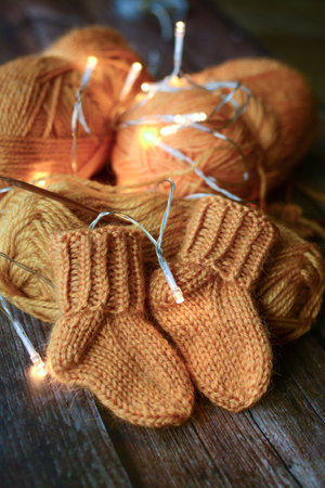 Knitted baby booties with Christmas lights on rustic wooden backgroundの写真素材