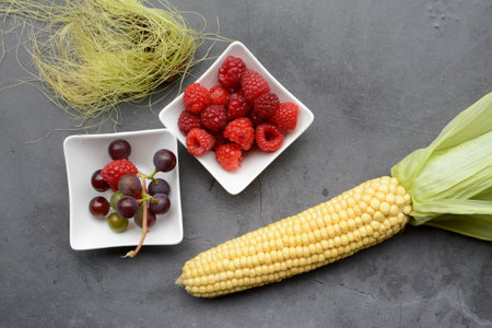 Fresh berries and corn on the cob in a bowl on a gray backgroundの写真素材