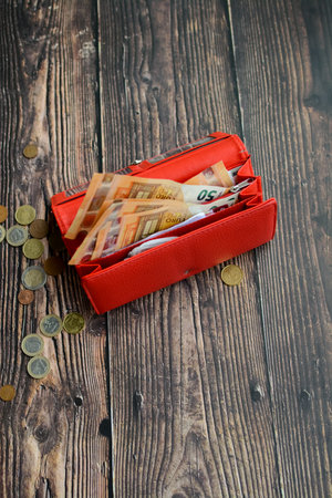 Red wallet with euro banknotes and coins on a wooden background.