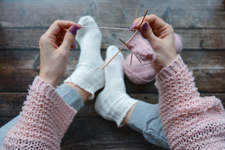 Female hands knitting woolen socks. Knitting needles and woolen socks on a wooden backgroundの写真素材