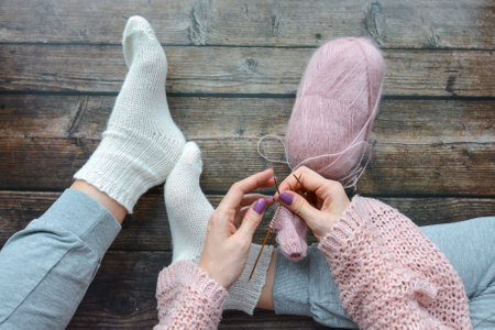 Hands of a young woman knitting on a wooden background. Knitting needles and woolen socksの写真素材
