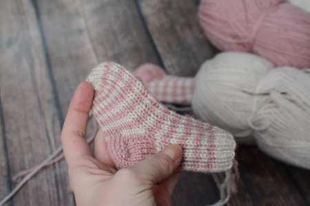 A woman's hand holds a woolen sock. Knitting needles and yarn on a wooden background.の写真素材