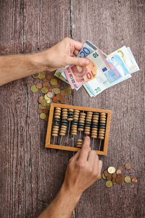 Hands counting money with abacus and euro banknotes on wooden backgroundの写真素材