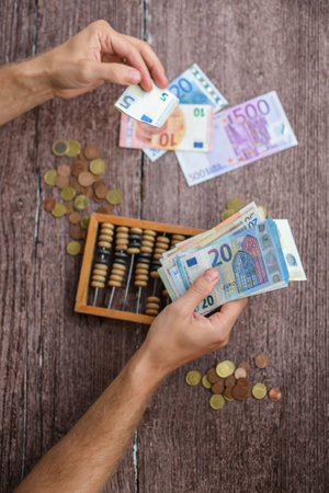 Hands counting euro banknotes and wooden abacus on wooden tableの写真素材