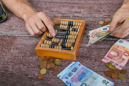 Man counting money with abacus, euro banknotes and coins on wooden tableの写真素材