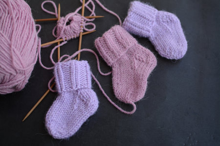 Knitted baby booties with knitting needles on a black background.の写真素材
