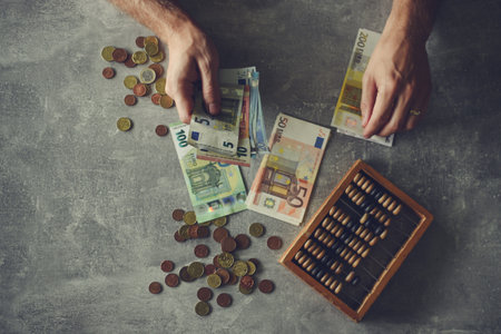 Businessman counting money with abacus and euro banknotes on grey background
