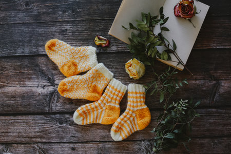 Pair of knitted socks with a book and flowers on a wooden backgroundの写真素材