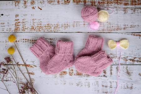 Knitted baby booties with woolen threads on white wooden background