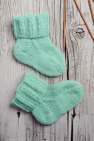 Green knitted socks and knitting needles on a white wooden background.