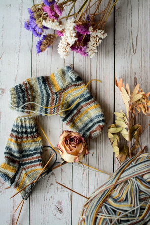 Woolen socks, yarn and dried flowers on white wooden backgroundの写真素材