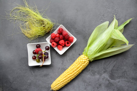 Fresh berries and corn on the cob on a gray background, top view