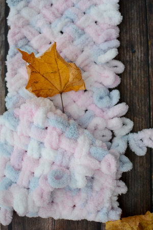 Knitted woolen scarf and autumn leaves on a wooden background.