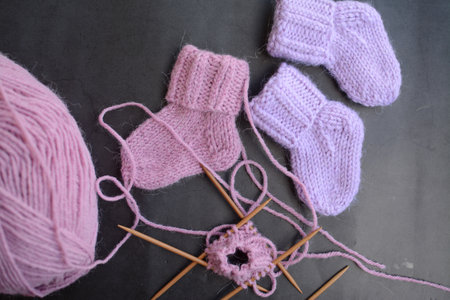Knitted baby booties and knitting needles on a gray background.の写真素材