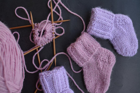 Knitted baby booties with knitting needles on a black background.の写真素材
