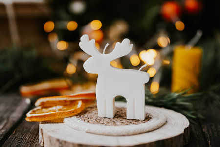 Soy wax candle, Christmas decoration, reindeer figurine on wooden board, bokeh lightsの写真素材