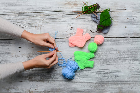 Cropped image of female hands knitting woolen socks on wooden background