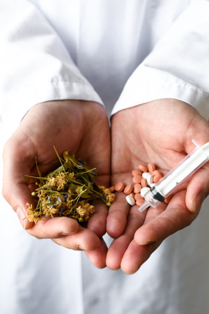 Male doctor holding a handful of pills, medicinal herbs and a syringe.の写真素材