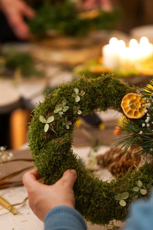 Hands decorating christmas wreath with moss and dried orangeの写真素材