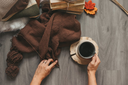 Female hands with a cup of coffee, books and a knitted sweater on a wooden background.の写真素材