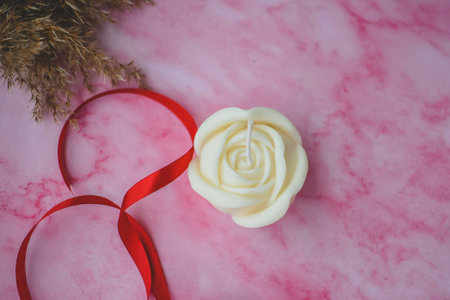White wax candle with red ribbon on pink backgroundの写真素材