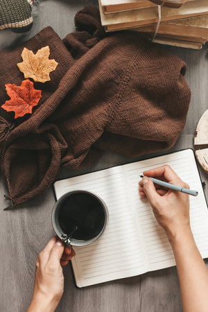 Female hands are writing in a notebook. Cup of coffee and autumn leaves.の写真素材