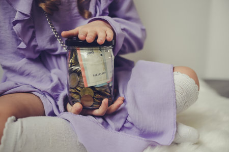 Little girl with money in a glass jar on the bed at homeの写真素材