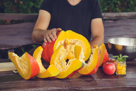 Hands of a man in a black T-shirt cut a pumpkin on a wooden tableの写真素材
