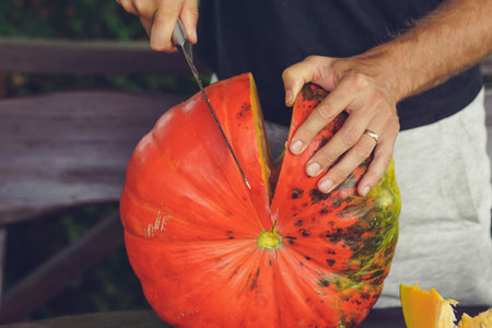 Hands of a man cutting a pumpkin with a knife on a wooden tableの写真素材