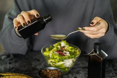 Woman in the kitchen preparing a salad. Close-up of a female hands holding a bottle of vegetable oil.の写真素材