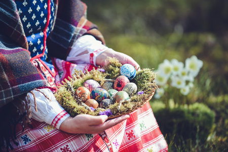 Easter eggs in a basket in the hands of a woman wearing traditional Lithuanian clothes in the forest.の写真素材
