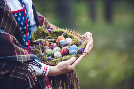 Easter eggs in a basket in the hands of a woman wearing traditional Lithuanian clothes in the forest.の写真素材
