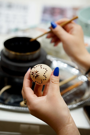 Close-up of a female hand painting a easter egg with a hot bee waxの写真素材