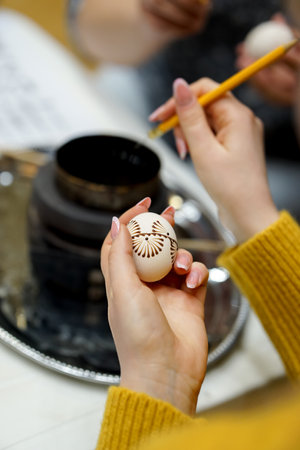 Close up of woman painting Easter egg, using burnt bees wax, with brush in her hands.の写真素材