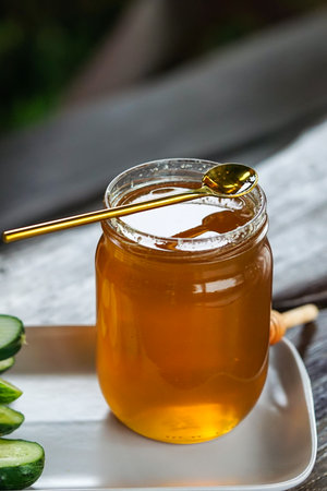 honey in a jar and fresh cucumbers on a wooden tableの写真素材
