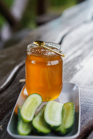 honey in a jar and fresh cucumbers on a wooden tableの写真素材
