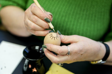 Woman painting Easter egg with bee wax in her workshop. Selective focus.の写真素材