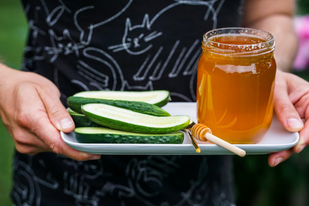 Hands holding a plate with cucumber slices and honey in the gardenの写真素材