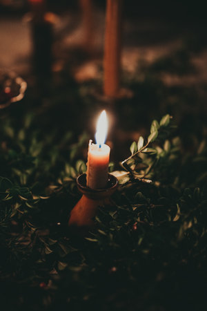 Burning candle in a candlestick on a background of green leavesの写真素材
