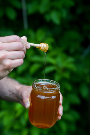 Honey dripping from a wooden honey dipper into a glass jarの写真素材