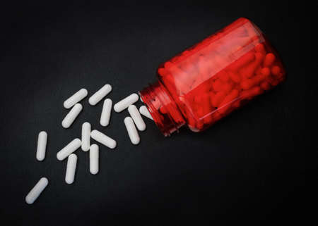 White medicine tablets or vitamins in a red bottle on a black backgroundの写真素材