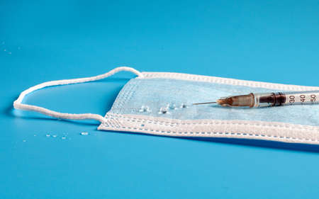 Insulin syringe with needle and medicine drops on a medical face mask. Pandemic photography in the...