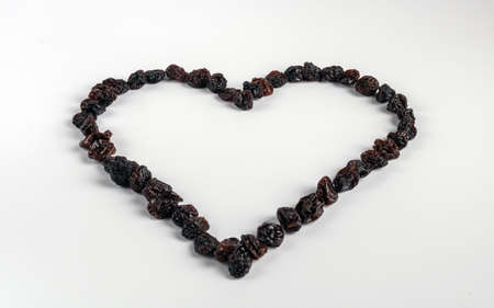 Healthy large raisins, arranged in the shape of a heart, because it helps to strengthen the heart, as well as are very tasty. Raisins are placed on a distinctly white background. Place for text.の写真素材