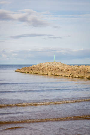 Dry, huge stones in the sea have dried up in the sun. A pier formed of hundreds of stones. Baltic Sea coast, waves. Blue sky, white clouds.の写真素材