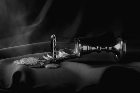 Glass cup with diamonds, crystals and a silver handle in a horizontal position. Money and coins are...