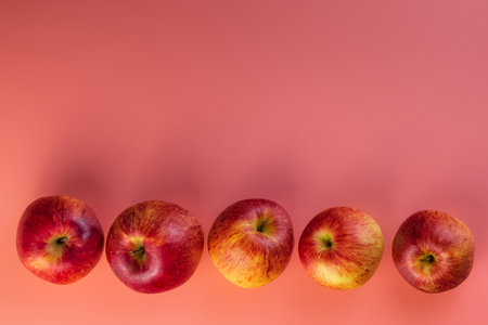 Five round, fresh, seductive red autumn apples. They fly in the air next to each other. Baby pink background. Unusually stylish wallpaper. A healthy diet.の写真素材