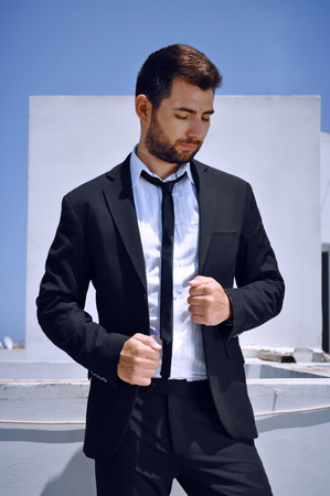 Attractive Spanish looking young man with a beard and dark hair and eyes is wearing a black suit and tie with a white shirt.の写真素材