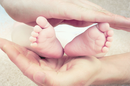 Tiny baby feet surrounded by fathers strong hands.の写真素材