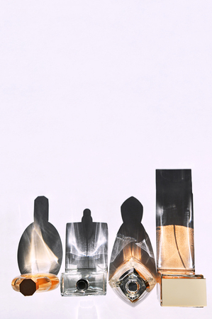 Transparent glass perfume bottles in different sizes and shapes standing in a row in bright light on white background omitting strong shadows.の写真素材